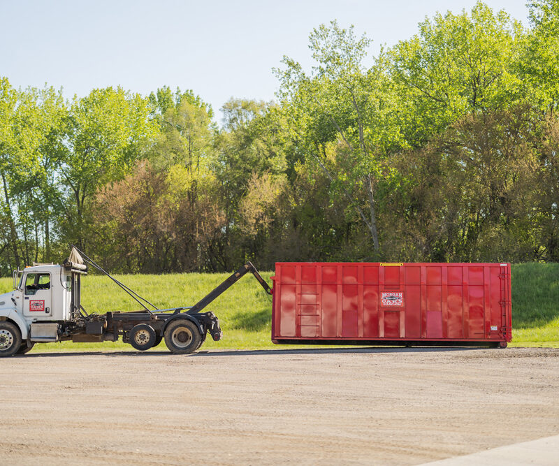 Morgan Oaks delivery truck hauling a dumpster rental