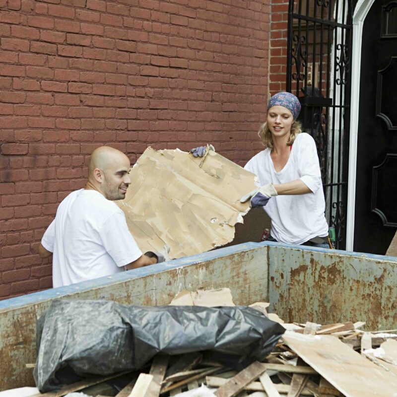 Photo of a couple throwing debris into a dumpster during a home renovation project.